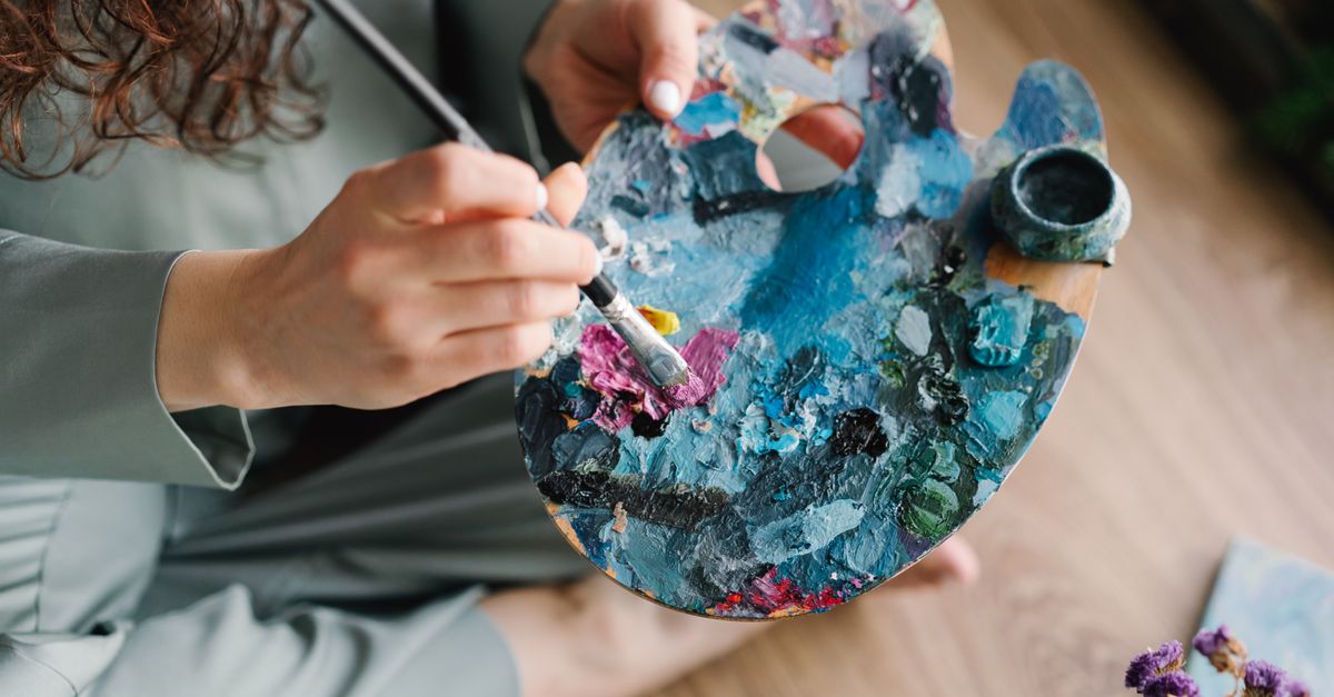 Close-up of hands painting on a colorful palette, showcasing creativity and artistry.